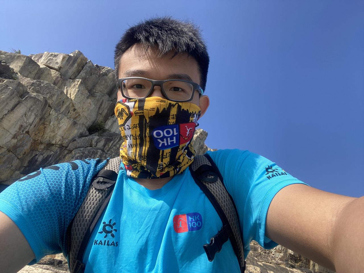 Athlete wearing face covering with HK100, Kailas blue shirt with rocky background
