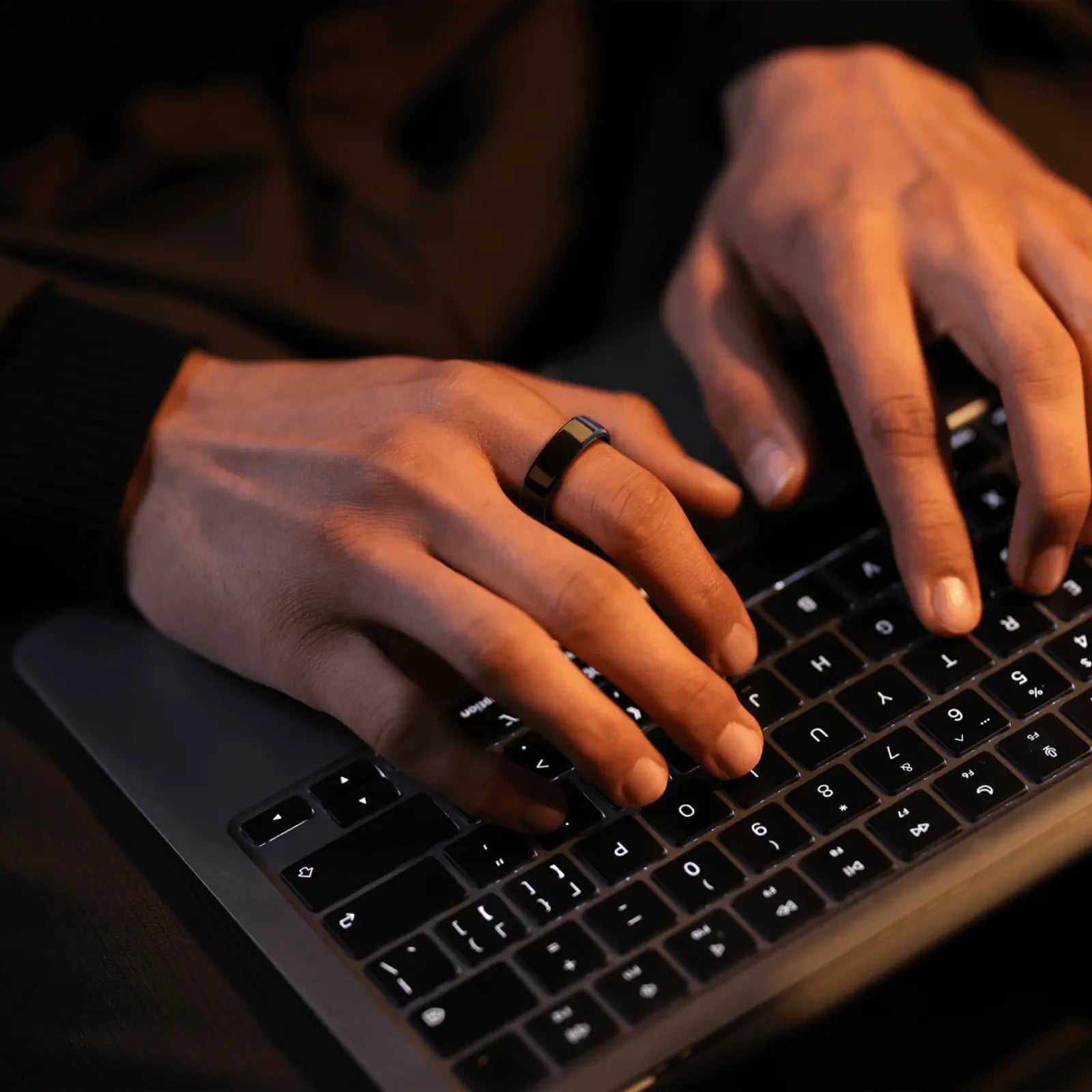 Person typing on laptop wearing a sleek smart ring. Promoting health tracking and sleep monitoring features.