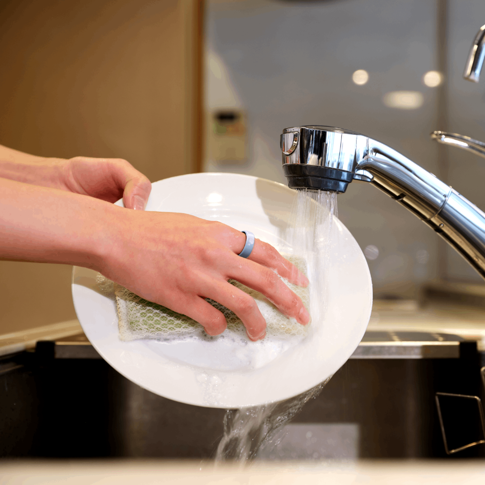 A person washes a plate in a sink, wearing a blue silicone protector ring. Focus on the lightweight, medical-grade material.