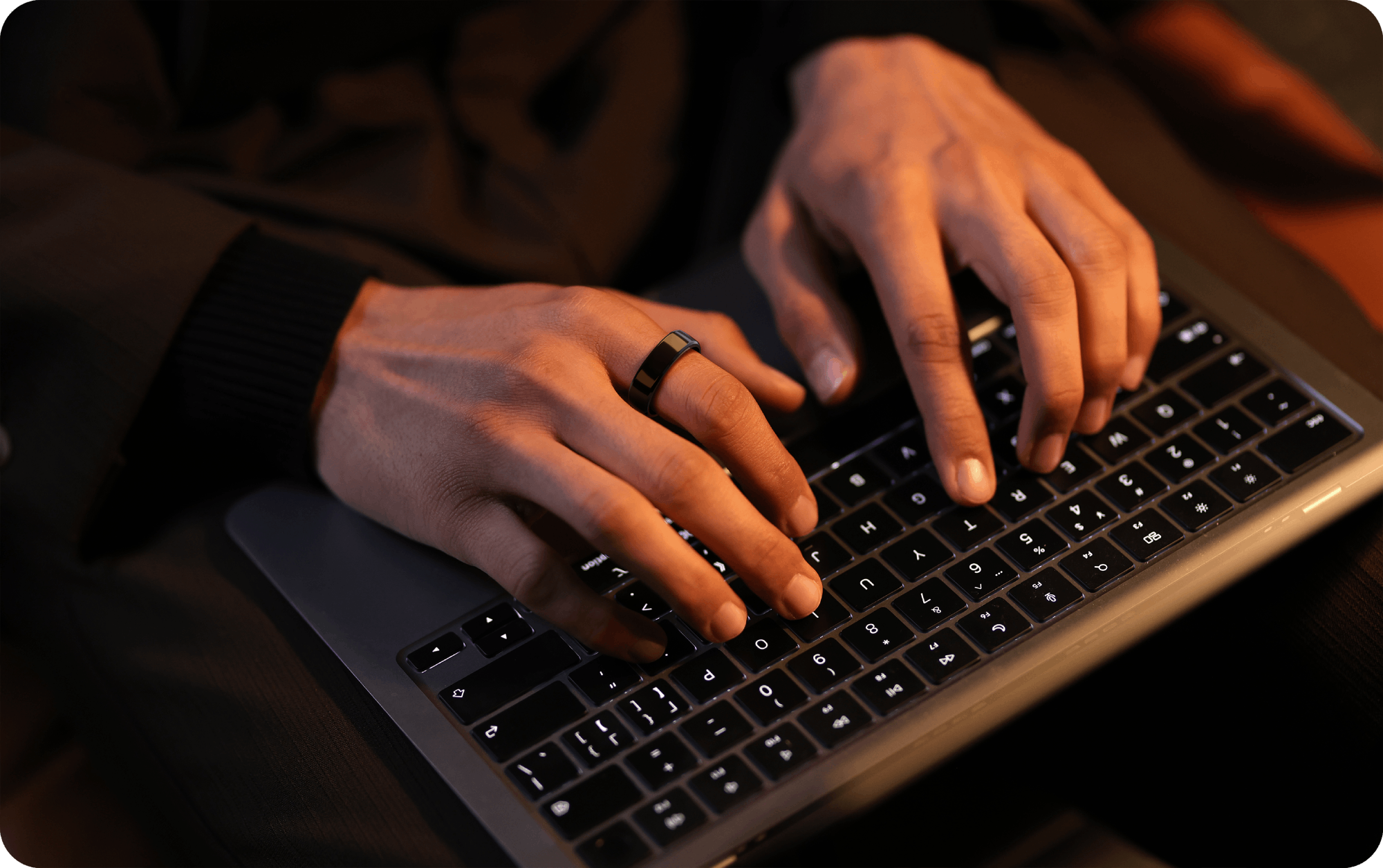 Black smart ring on finger, typing on laptop, emphasizing health tracking technology and modern tech.