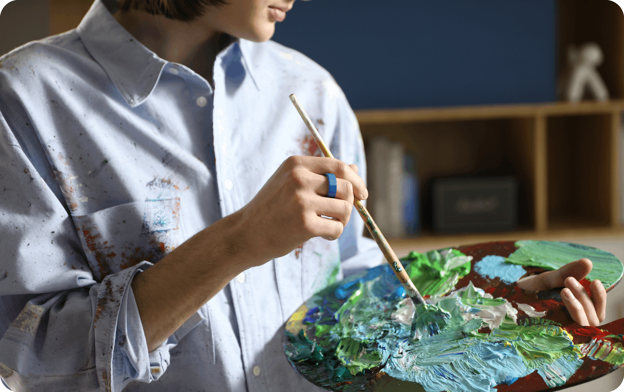 Blue smart ring on artist's finger, holding paintbrush and palette, creative lifestyle.