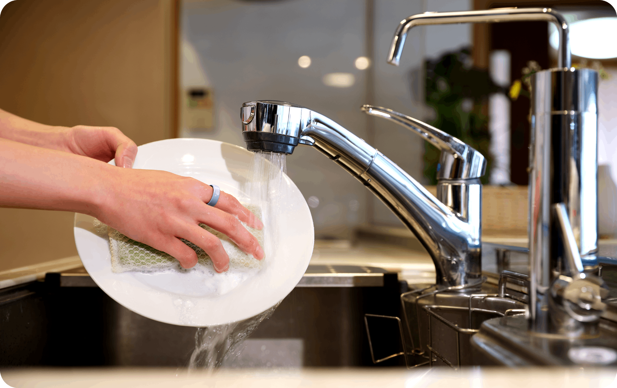 Person washing a white plate with a light blue smart ring, modern health tech.