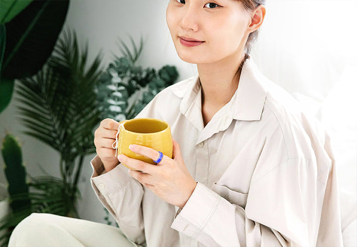 Woman wearing blue smart ring, showcasing design while holding a yellow cup