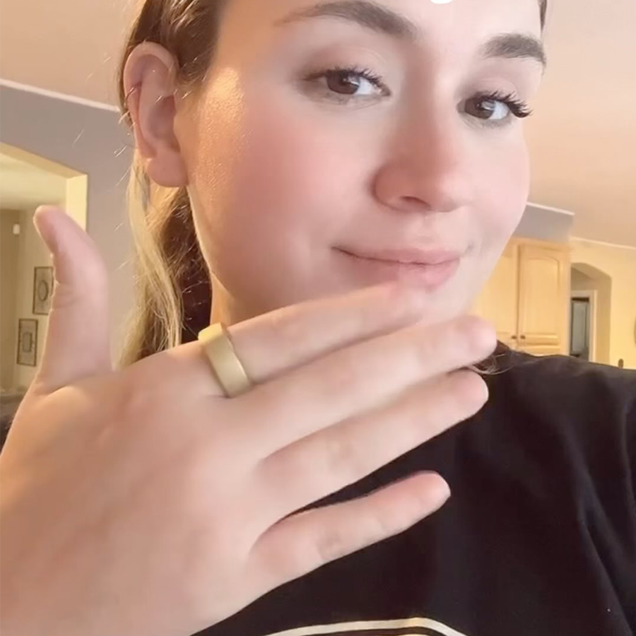 Woman smiling wearing a gold smart ring, black shirt, and showing hand gesture